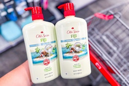 person holding 2 large bottles of old spice body wash over a cart