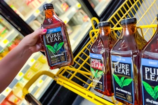hand holding up a bottle of pure leaf tea next to a yellow shopping cart