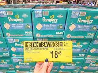 person holding a sign for $18.48 sale price on pampers baby wipes in front of boxes of wipes