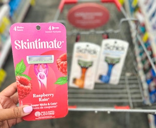 hand holding pack of Skintimate razors in front of shopping cart with Schick razors inside