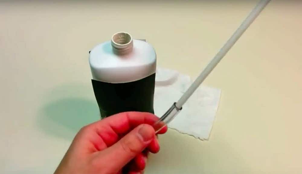 Person attaching a piece of vinyl tubing to the end of a lotion bottle pump.