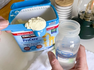 A person putting a scoop of Kirkland powdered baby formula into a bottle