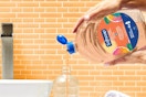 In a peach bathroom, two hands pour a Softsoap Antibacterial refill into a sink dispenser.