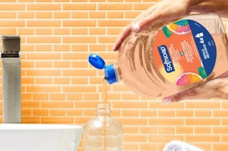 In a peach bathroom, two hands pour a Softsoap Antibacterial refill into a sink dispenser.