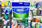 hand holding bag of floss picks in front of oral hygiene product shelves