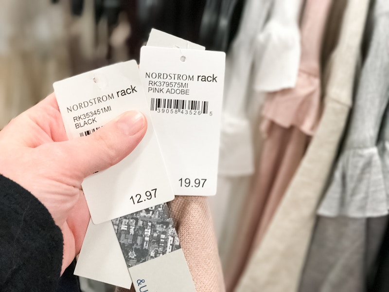 A person holding three price tags all with Nordstrom on the tag along with 3 red price tag stickers for Nordstrom Rack.