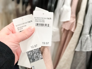 A person holding three price tags all with Nordstrom on the tag along with 3 red price tag stickers for Nordstrom Rack.