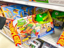 hand grabbing a hot wheels city t-rex set off a target shelf