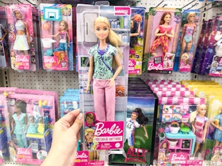hand holding barbie in front of barbie store display