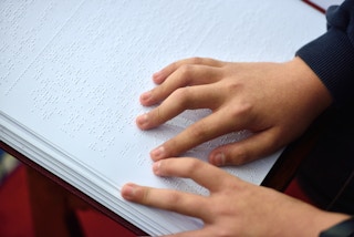 A child's hands going over the page of a braille book.