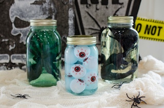 Large mason jars filled with water, food coloring, and dish soap, containing dollar tree plastic eyeballs, spider, and snake.