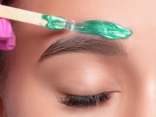 A woman getting her eyebrows waxed with aloe wax beads.