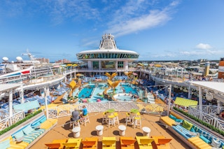 The top of a Royal Caribbean cruise ship with a balcony looking down over a pool with people and lounge chairs.