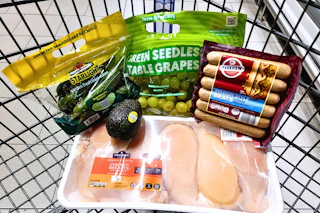 grapes, mini cucumbers, bratwursts, avocado, and chicken breasts in a cart