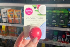 A hand holding Eos lip balm in a store aisle.
