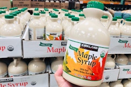 Kirkland Maple Syrup held in front of pallet of maple syrup