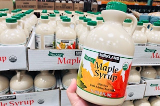 Kirkland Maple Syrup held in front of pallet of maple syrup