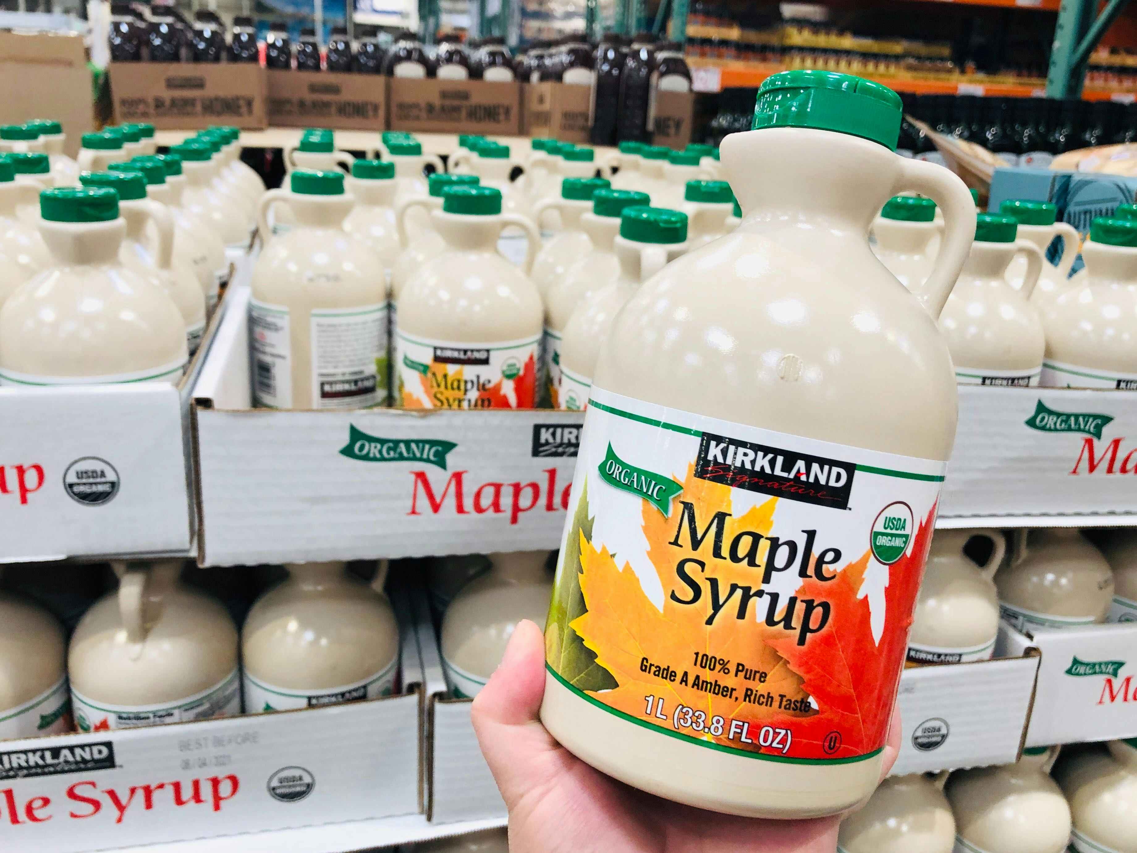 Kirkland Maple Syrup held in front of pallet of maple syrup