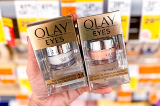 hand holding two eye creams in front of store shelf with sale tags in background