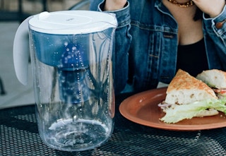 blue Pur water filtration pitcher next to woman with food