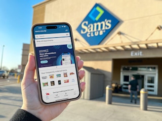 Someone holding up a phone displaying the Sam's Club app in front of Sam's Club