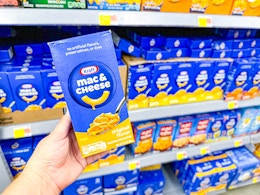 hand holding a box of Kraft Mac n Cheese in front of the noodle aisle