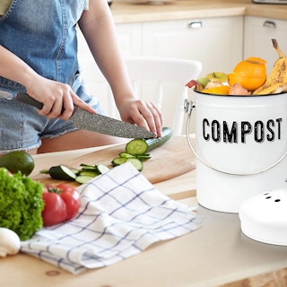 A person chopping vegetables in a kitchen near a farmhouse compost bin.