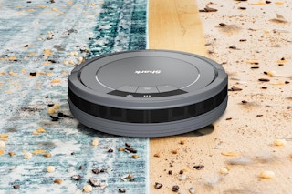 A Shark robot vacuum propels itself along a rug and floor, cleaning them both