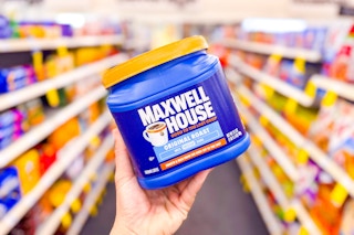 person holding a container of maxwell house coffee in an aisle