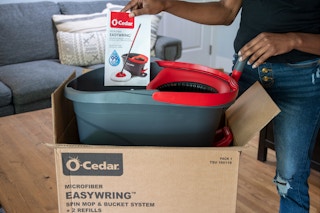 a person pulling out an O-Cedar Mop from a cardboard box in a room