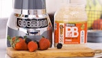 A tub of PBfit peanut butter powder next to a blender