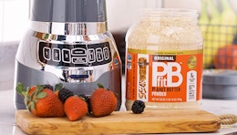 A tub of PBfit peanut butter powder next to a blender