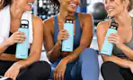 3 women in a gym with holding blue water bottles