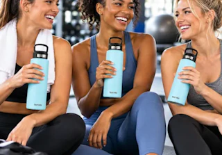 3 women in a gym with holding blue water bottles
