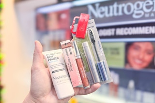 person holding neutrogena lip gloss, eyeshadow, primer, and mascara