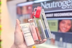person holding neutrogena lip gloss, eyeshadow, primer, and mascara