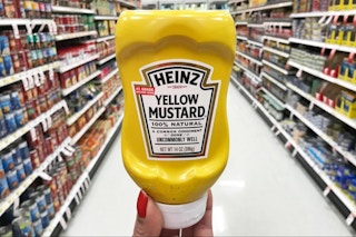 a hand holding a bottle of mustard in a store aisle 