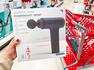 hand holding a sharper image massage gun in front of a target cart