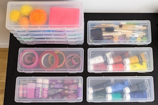 Ten clear plastic storage boxes are arranged on a black surface. Five are lined up and five are stacked.