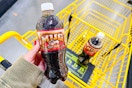 hand holding a mug root beer next to a yellow shopping cart