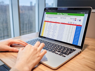 A person using a laptop displaying the 90 Day Ticker website for cruise deals.