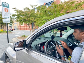 a man sitting in the car on his phone parked in curbside pickup outside of dicks sporting goods