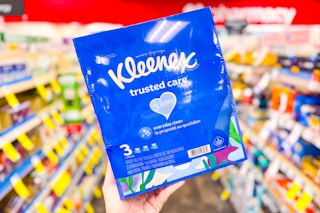 person holding a 3-pack of kleenex tissues in an aisle