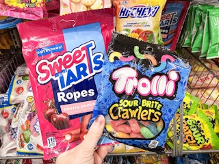 person holding sweetarts and trolli candy in front of a candy display