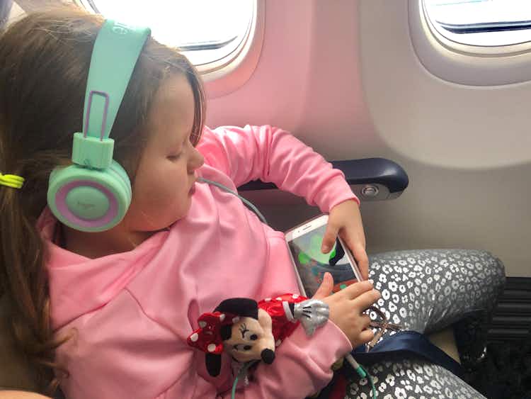 A little girl watches a movie on her phone and holds a Minnie Mouse doll on an airplane.