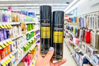 hand holding two cans of hair spray in store beauty aisle
