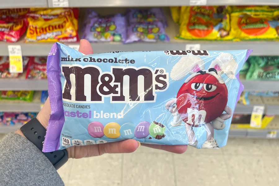 person holding a bag of m&ms candy by the shelf