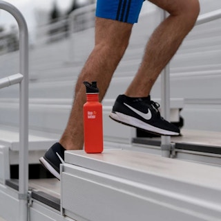 A man running on stairs, with an orange Klean Kanteen water bottle placed nearby.