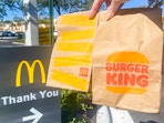 A person holding a McDonald's and Burger King to-go bag in one hand next to a sign that reads "thank you" with a McDonald's golden arch ...