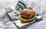 A Starbucks Impossible breakfast sandwich sitting on its bag on a striped cushion.